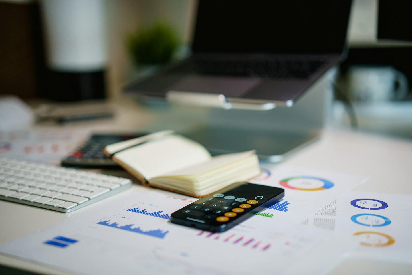 Laptop, Tastatur, Notizbuch und Smartphone auf einem Schreibtisch mit Finanzdiagrammen.